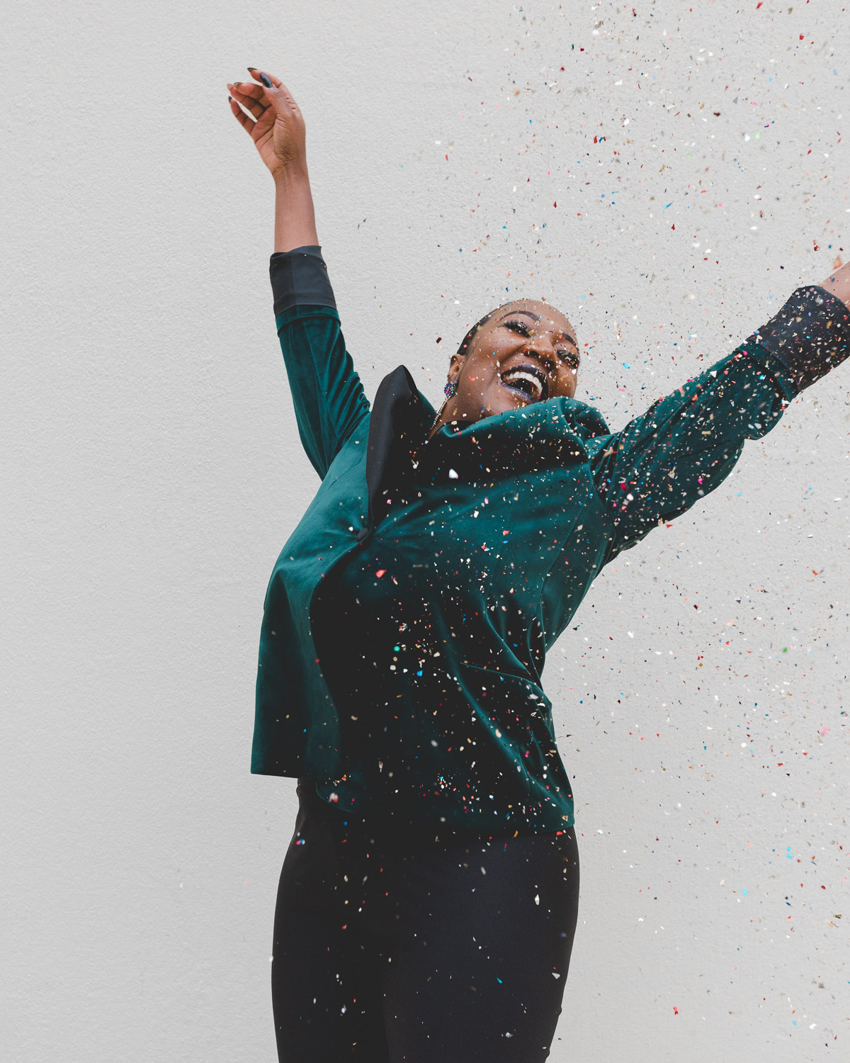 Woman looking happy, jumping up with her arms up in the air and confetti raining down